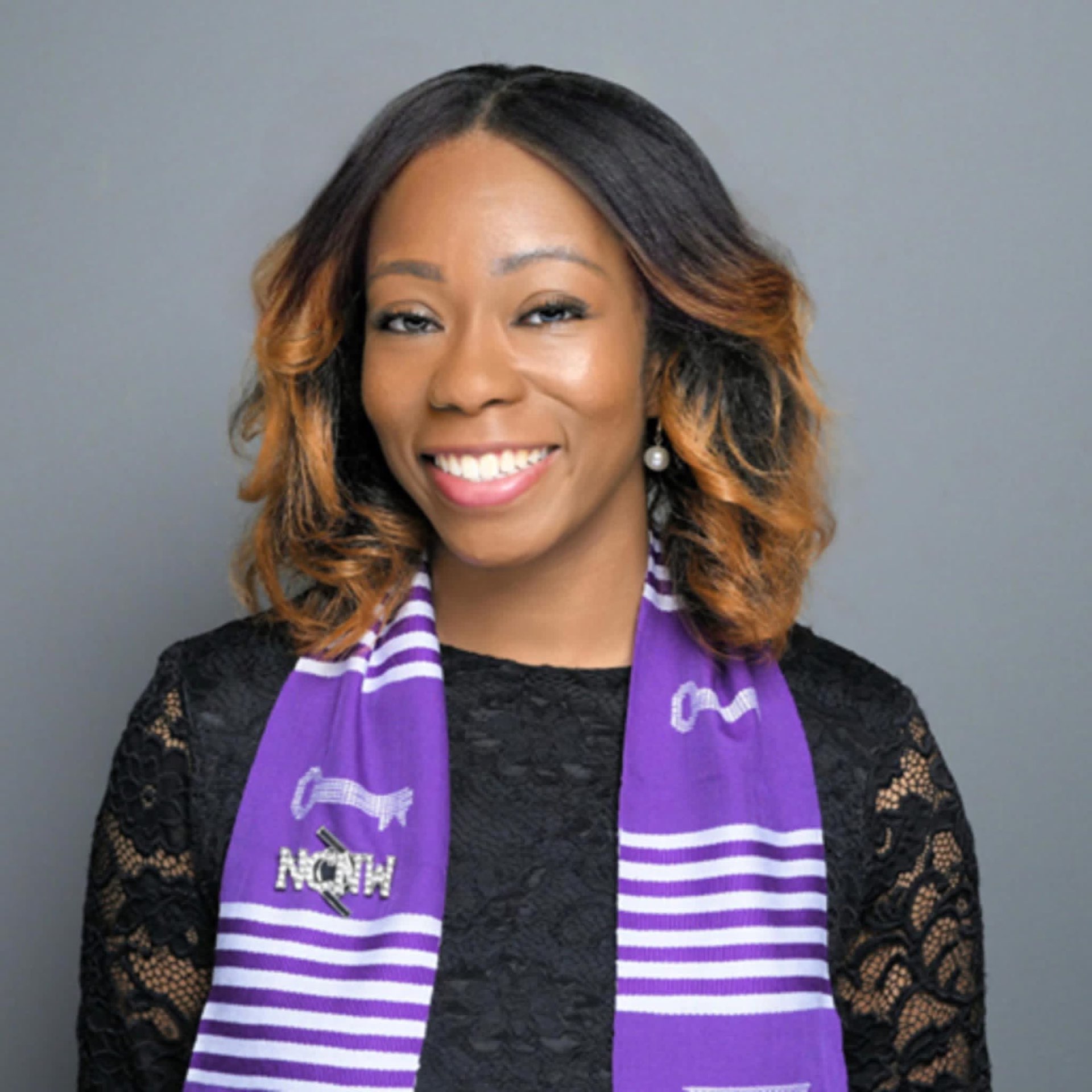 Coach Rena smiling in a black lace top and purple kente stole